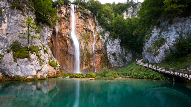 Discover the serenity of Plitvice Lakes National Park with a vibrant waterfall and wooden bridge, perfect for travel and nature enthusiasts