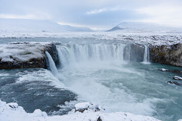 A stunning winter landscape featuring a waterfall cascading into a river.