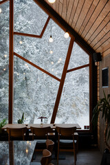 View of snow covered trees from the inside of a restaurant with wood walls.