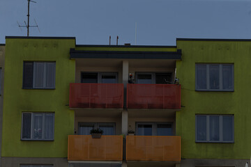 symmetrical green facade with colorful balconies and centered windows, balanced composition and flat daylight conveying community housing character for brochure and social research imagery