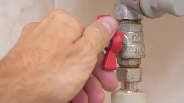 Red valve on cold water pipe to boiler for heating. Boiler heats water from cold water supply system. Man turns red valve and cut off the cold water supply to boiler