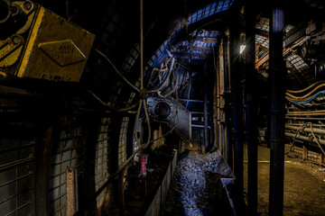 Naklejka premium Deep underground, a long mining tunnel stretches into darkness as massive coal-cutting machines carve through the rock. The scene captures the intense atmosphere, heavy industry, and powerful equipmen
