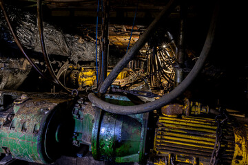 Underground coal mining scene with massive industrial machines operating inside long tunnels and narrow galleries. Dim light, heavy equipment, and rough walls show the harsh conditions of subterranean