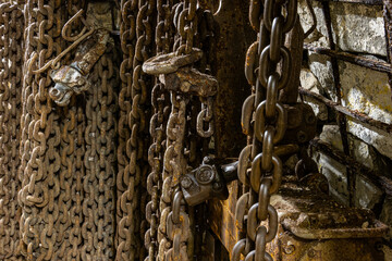 Heavy tools and equipment inside an underground mine, with steel chains, pneumatic hoses, and supply lines in active use. The scene shows industrial work conditions, mining technology, and harsh subte