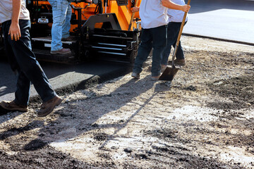 Construction workers lay asphalt using heavy machinery while others prepare surface