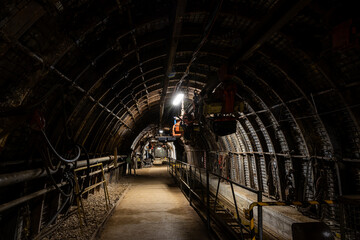 Underground coal mining scene with massive industrial machines operating in long, dark tunnels. Narrow passages and heavy equipment illustrate industrial labor, energy production, and harsh working co