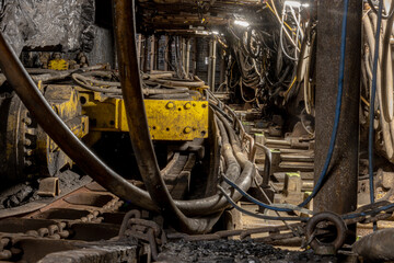 Underground coal mining scene with massive industrial machines operating inside long tunnels and narrow galleries. Dim light, heavy equipment, and rough walls show the harsh conditions of subterranean