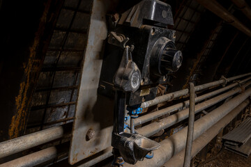 Heavy tools and equipment inside an underground mine, with steel chains, pneumatic hoses, and supply lines in active use. The scene shows industrial work conditions, mining technology, and harsh subte