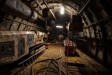 Coal miners work deep underground in a dark, rugged mine, illuminated only by headlamps and...