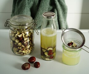 The image shows glass jar filled with a light brown, slightly cloudy liquid — homemade laundry detergent made from horse chestnuts.