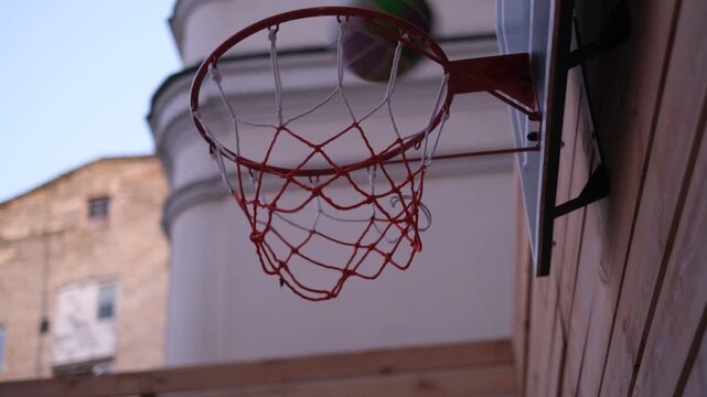 Ball goes through basketball hoop on outdoor street court in the evening close-up side view