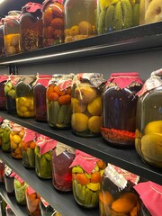 Preserved fruits and vegetables in big jars lined up on black wooden shelves