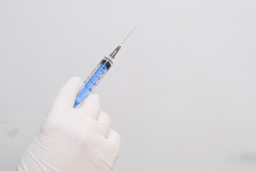 A gloved medical professional&rsquo;s hand holding a syringe against a white background. Concept A sterile tool prepared for clinical use.