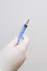 A gloved medical professional&rsquo;s hand holding a syringe against a white background. Concept A sterile tool prepared for clinical use.