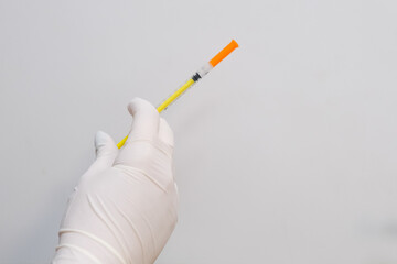 A gloved medical professional&rsquo;s hand holding a syringe against a white background. Concept A sterile tool prepared for clinical use.