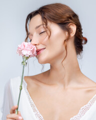 Fototapeta premium Elegant Beauty Portrait Of Woman Smelling Pink Carnation In White Dress