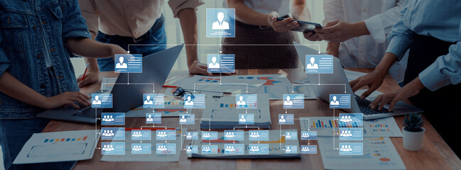A diverse group of professionals collaborates in a meeting, reviewing an organizational chart on a digital interface while analyzing data and discussing strategies. Trope