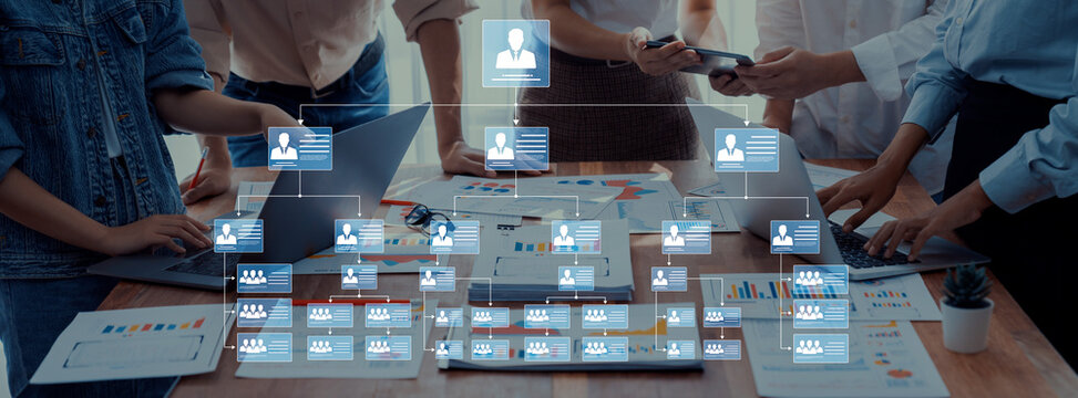 A diverse group of professionals collaborates in a meeting, reviewing an organizational chart on a digital interface while analyzing data and discussing strategies. Trope