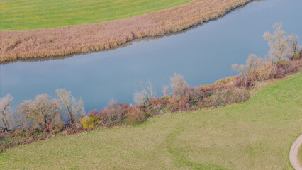 Blick auf einen ruhigen Fluss mit gr&uuml;nem Ufer und bunten B&uuml;schen im Fr&uuml;hling