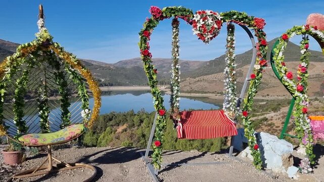 Decorative photo frames, including heart-shaped ones, set up for visitors to pose with the scenic Lac du Barrage Sed Nakhla dam in Zinat, Morocco, framed by mountains between Tetouan and Chefchaouen.