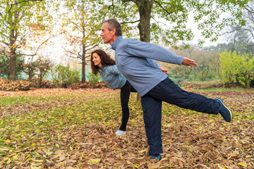 Mature couple balancing on one leg, practicing tai chi in an autumn park with fallen leaves