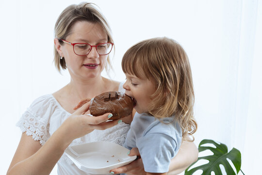 A mother giving her child a chocolate-glazed donut, an unhealthy feeding practice with food full of sugar.