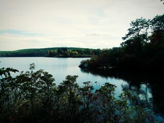 A clear fall day with blue sky on a lake nestled in a forest with vibrant fall foliage.