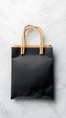 A simple black paper shopping bag with twisted rope handles sits centered on a textured white surface.