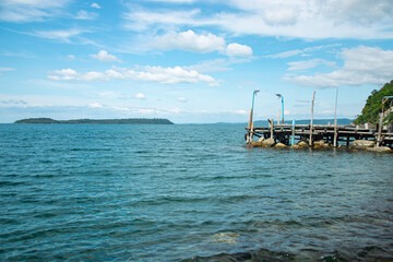 Obraz premium A view of a calm ocean with a distant island, pier, and cloudy sky. Koh Sdach, Cambodia
