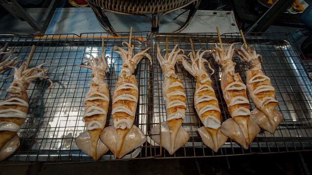 Grilled squid or pusit on skewers lined up on a metal grill, showcasing a delicious seafood market treat. Dumaguete, Philippines