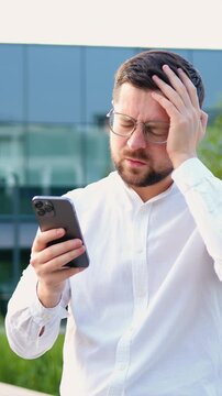 Single sad man in white shirt checking mobile phone walking in city at modern glass building background, indoors