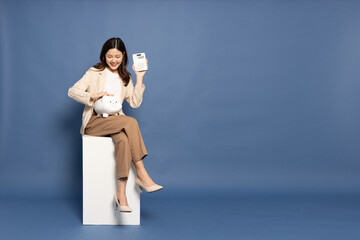 Happy young Asian woman holding calculator and piggy bank isolated on blue background, Business and financial concept