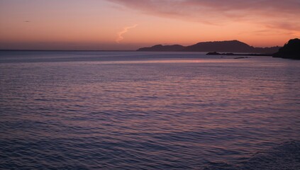 Obraz premium Sunlight reflects on calm water at dusk with a dark silhouette of the shoreline, tranquility of nature