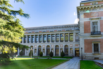 El Prado Museum on a sunny spring morning, showcasing elegant neoclassical architecture, grand statues, and lush green trees framing its bright, inviting façade with added charm
