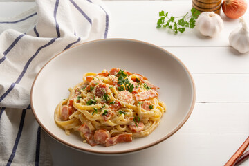 Fettuccine pasta with creamy carbonara sauce with pork sausage and bacon in a plate.