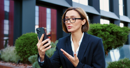Focused mature woman having online meeting sitting on a bench near office building, Middle aged businessman using smartphone while talking on a video call.