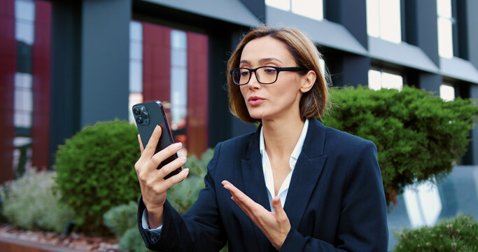 Focused mature woman having online meeting sitting on a bench near office building, Middle aged businessman using smartphone while talking on a video call.