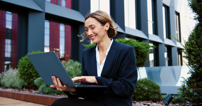 Elegant woman freelancer browsing surfing internet Businesswoman typing text on laptop sitting street bench close up. Beautiful business lady working remotely at computer outdoors vertically shot.