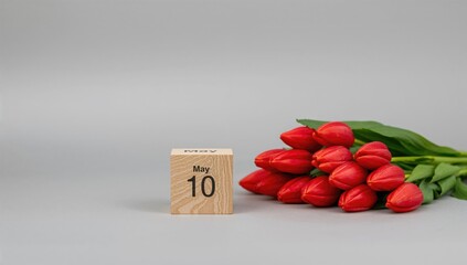 May 10 displayed on wooden blocks, accompanied by red tulips on a gray backdrop, seasonal change