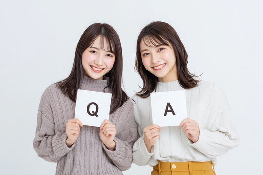 「Q」と「A」のカードを持って笑顔で並ぶ二人の若い女性（質問、回答、コピースペース） / Two young women smiling and standing side by side holding "Q" and "A" cards (Question, answer, copy space)