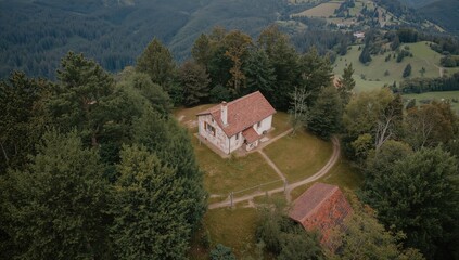 Obraz premium High-angle view of a solitary building on a hillside, surrounded by tall trees and a pathway, showcasing erosion risk