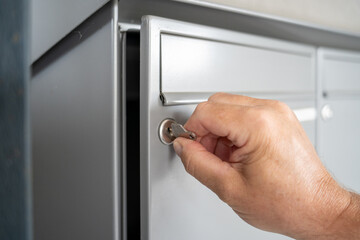 Hand opens a mailbox with a key in a row of grey metal mailboxes with drop slots for mail, correspondence, letters, utility bills