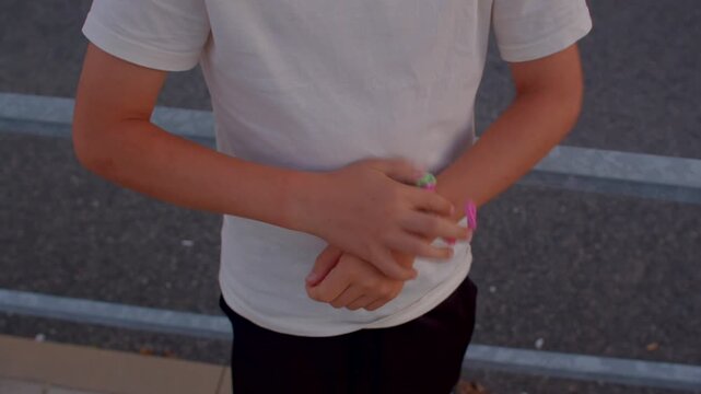 young crafter preparing friendship bracelet for friend, twisting neon beads around wrist on pavement rail,