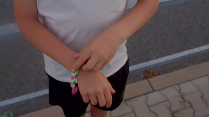 child weaving neon friendship bracelet on wrist with focused fingers, colorful beads and string, pavestone - Powered by Adobe