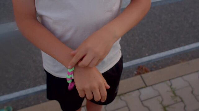 child weaving neon friendship bracelet on wrist with focused fingers, colorful beads and string, pavestone
