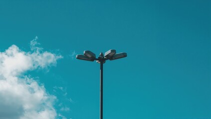 Three light fixtures mounted on a tall pole against a bright blue sky, providing illumination below, seasonal change