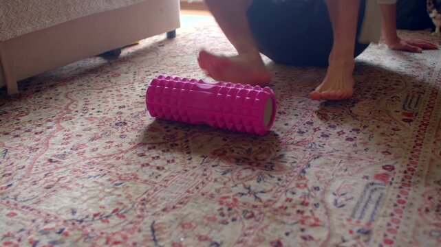 white man rolling foot on roller, spiky pink roller on patterned carpet, focused plantar fascia massage,