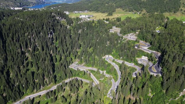 Aerial view of Maloja Pass road in the Swiss Alps. Dangerous serpentine road in high mountains, beautiful nature of forests and peaks between which cars drive.