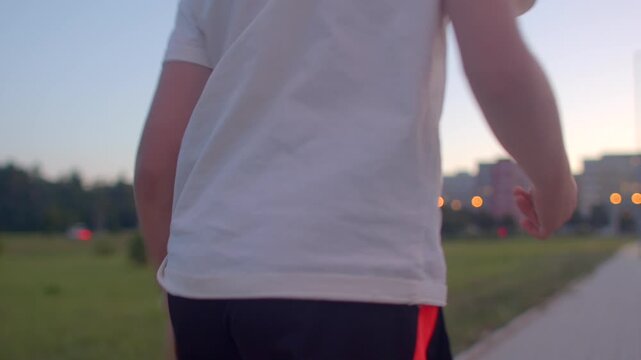 white teen walking along path dusk casual t-shirt black shorts crocs pavement bokeh lights distant skyline