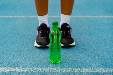 Athlete standing on a blue running track with a green plastic water bottle
